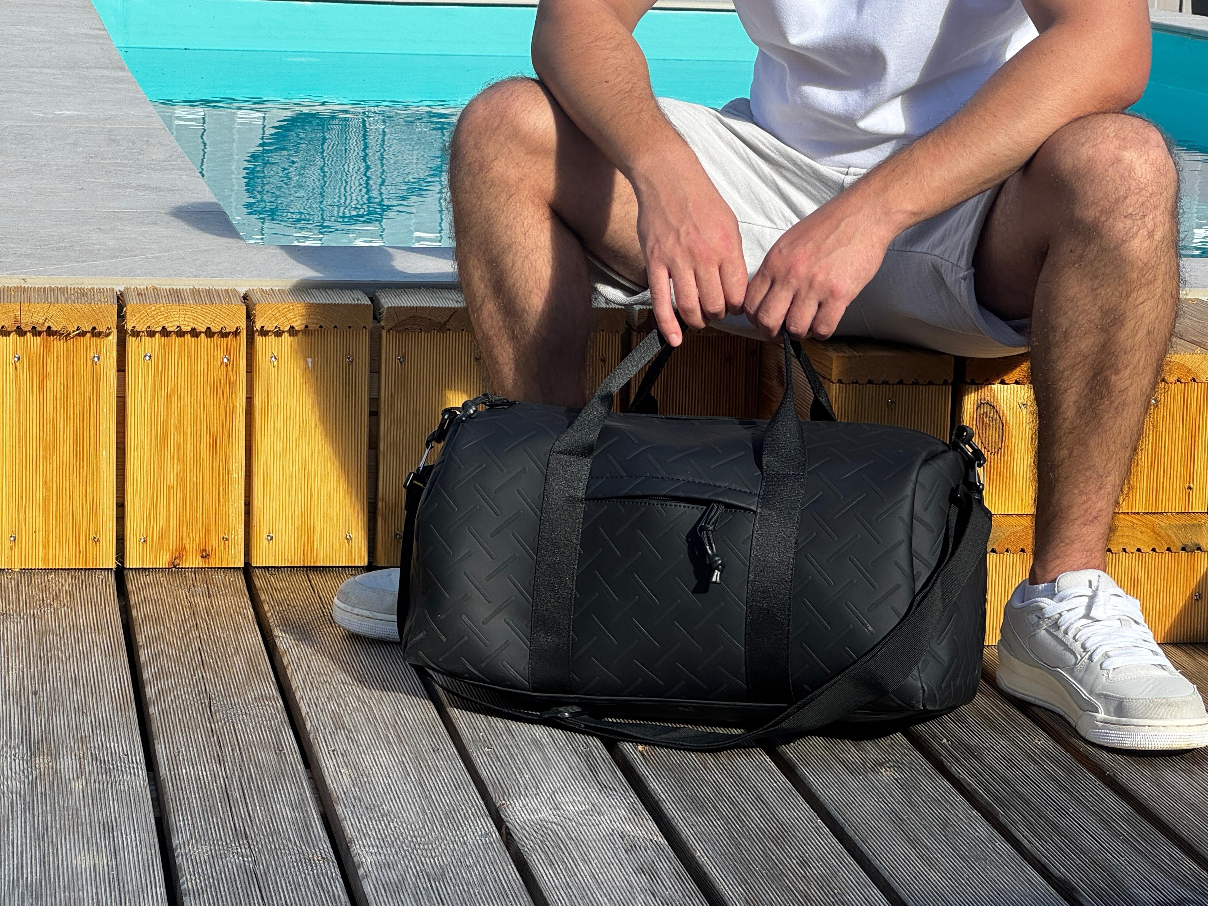 LS Fashion black weekender bag held by man sitting by pool on wooden deck