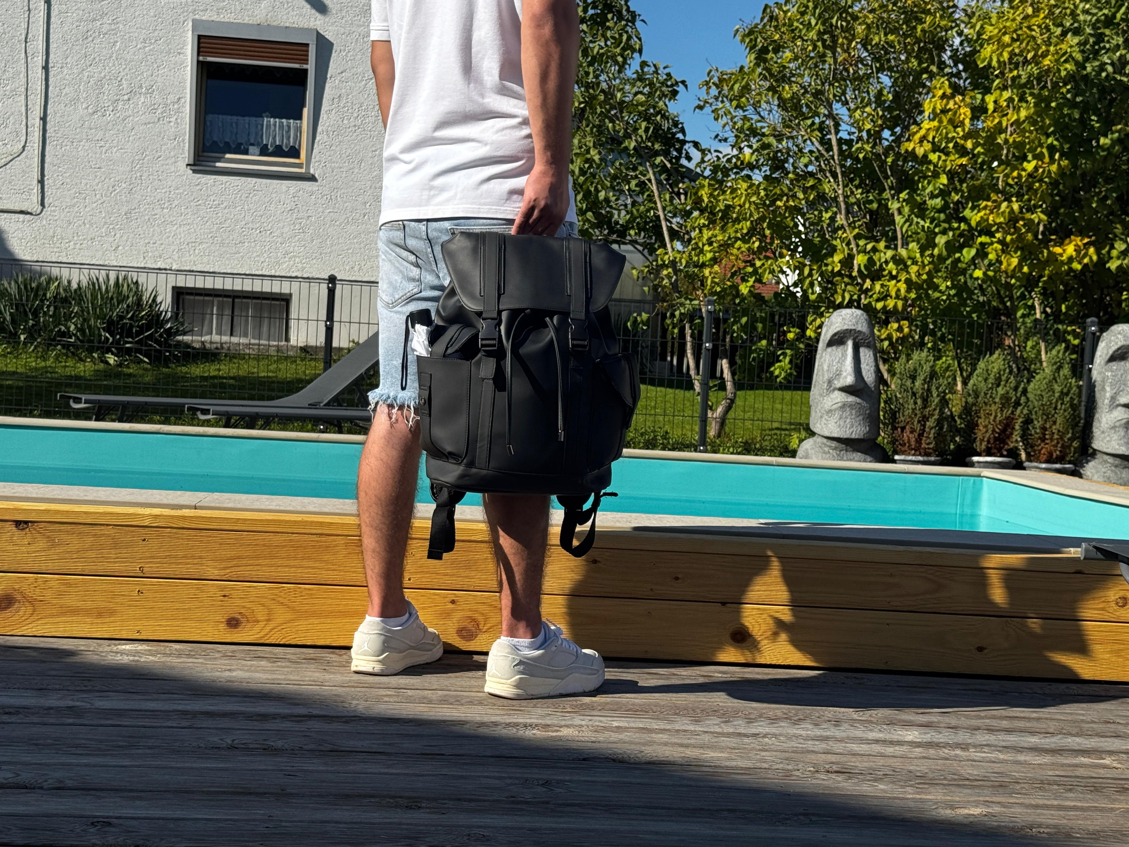 LS Fashion black leather rucksack weekender held by man in white shirt and shorts near pool