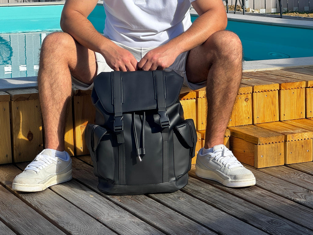 LS Fashion black leather rucksack placed between legs of man sitting on wooden deck by pool