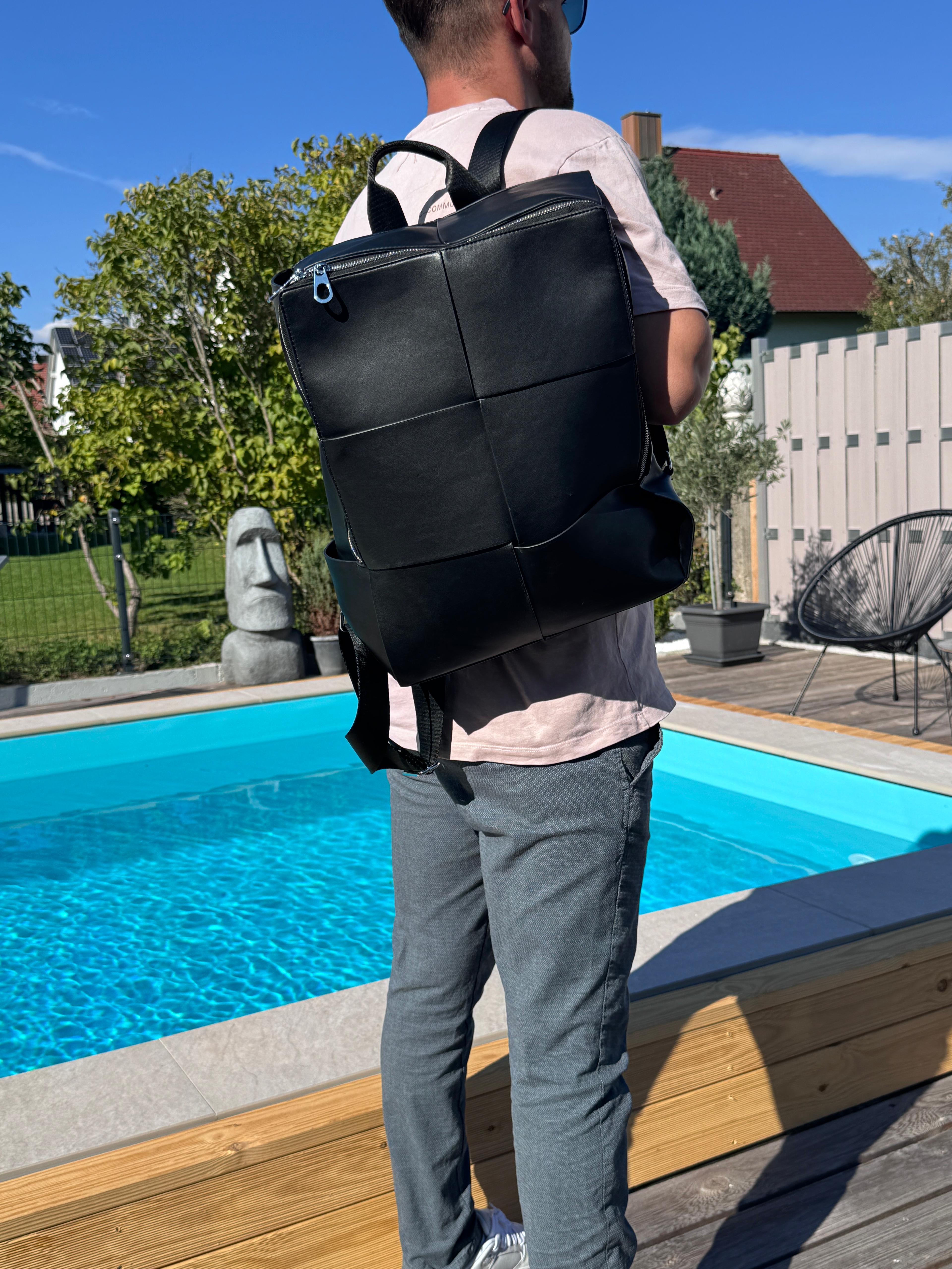 Man wearing a black leather rucksack by LS Fashion standing near a pool in casual outfit